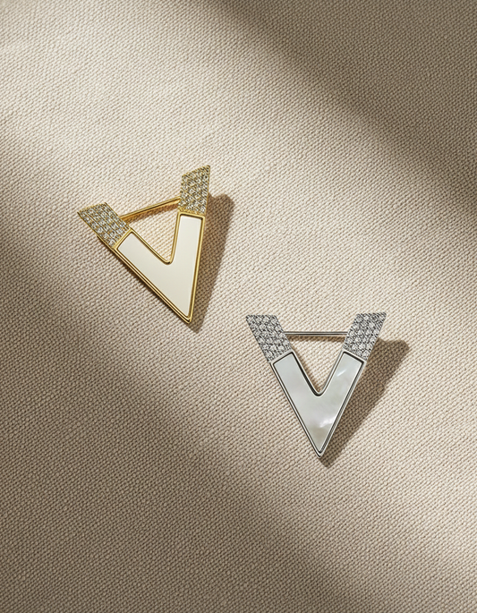 Elegant minimalist V-shaped gold and silver brooch styled on a black blazer, soft beige background, modern geometric design