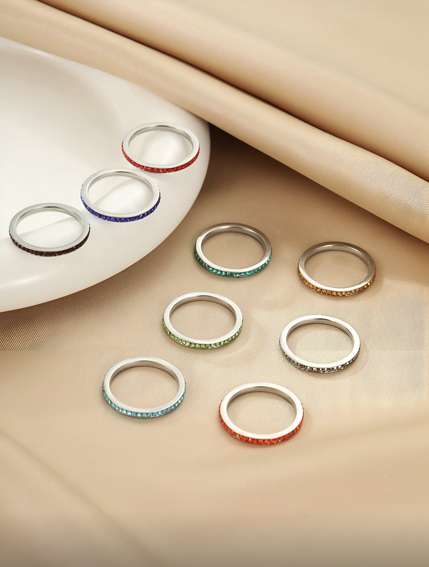 9-piece rainbow stacking rings set in vibrant colors on a soft beige background, minimalist modern jewelry, HAVA Store aesthetic