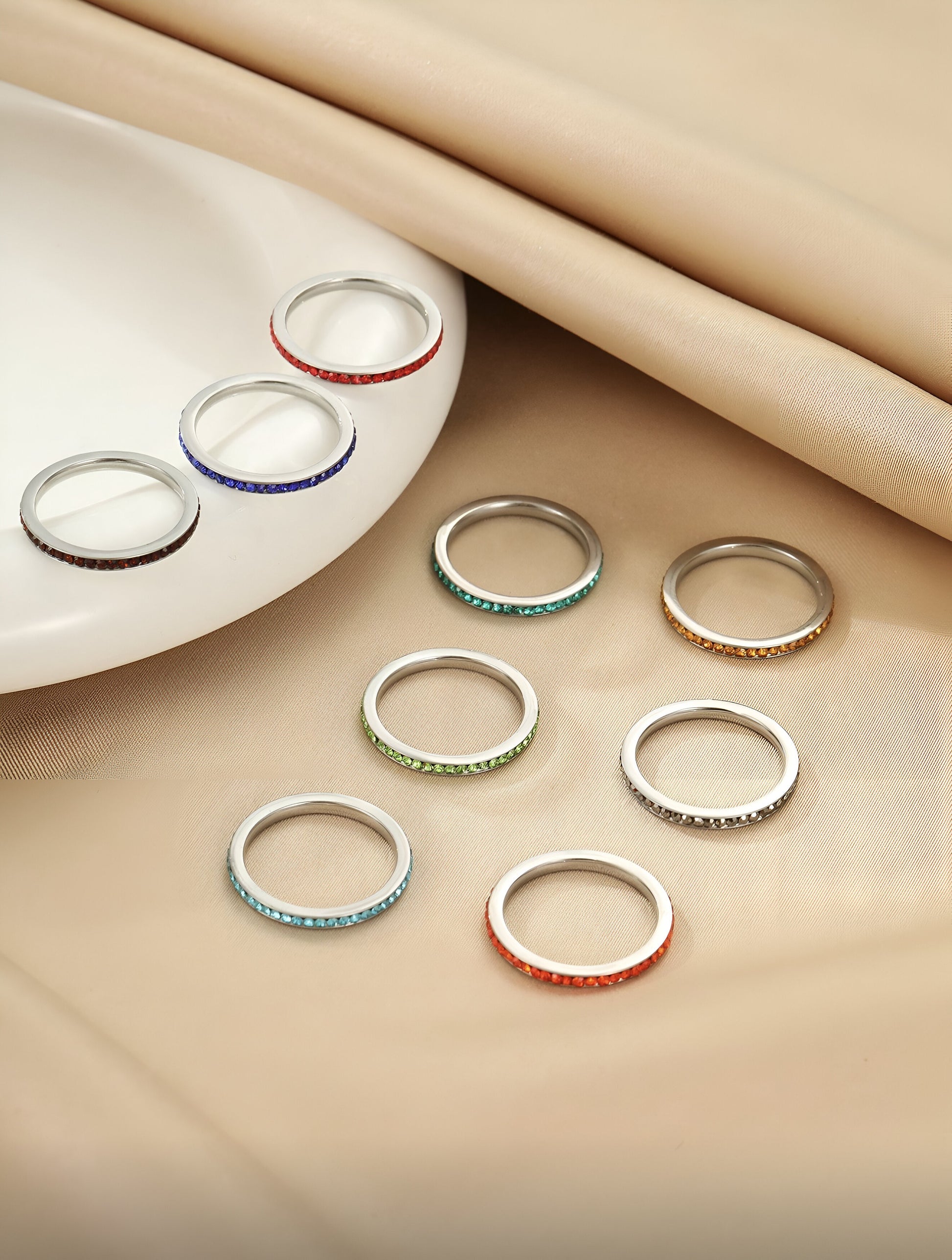 9-piece rainbow stacking rings set in vibrant colors on a soft beige background, minimalist modern jewelry, HAVA Store aesthetic
