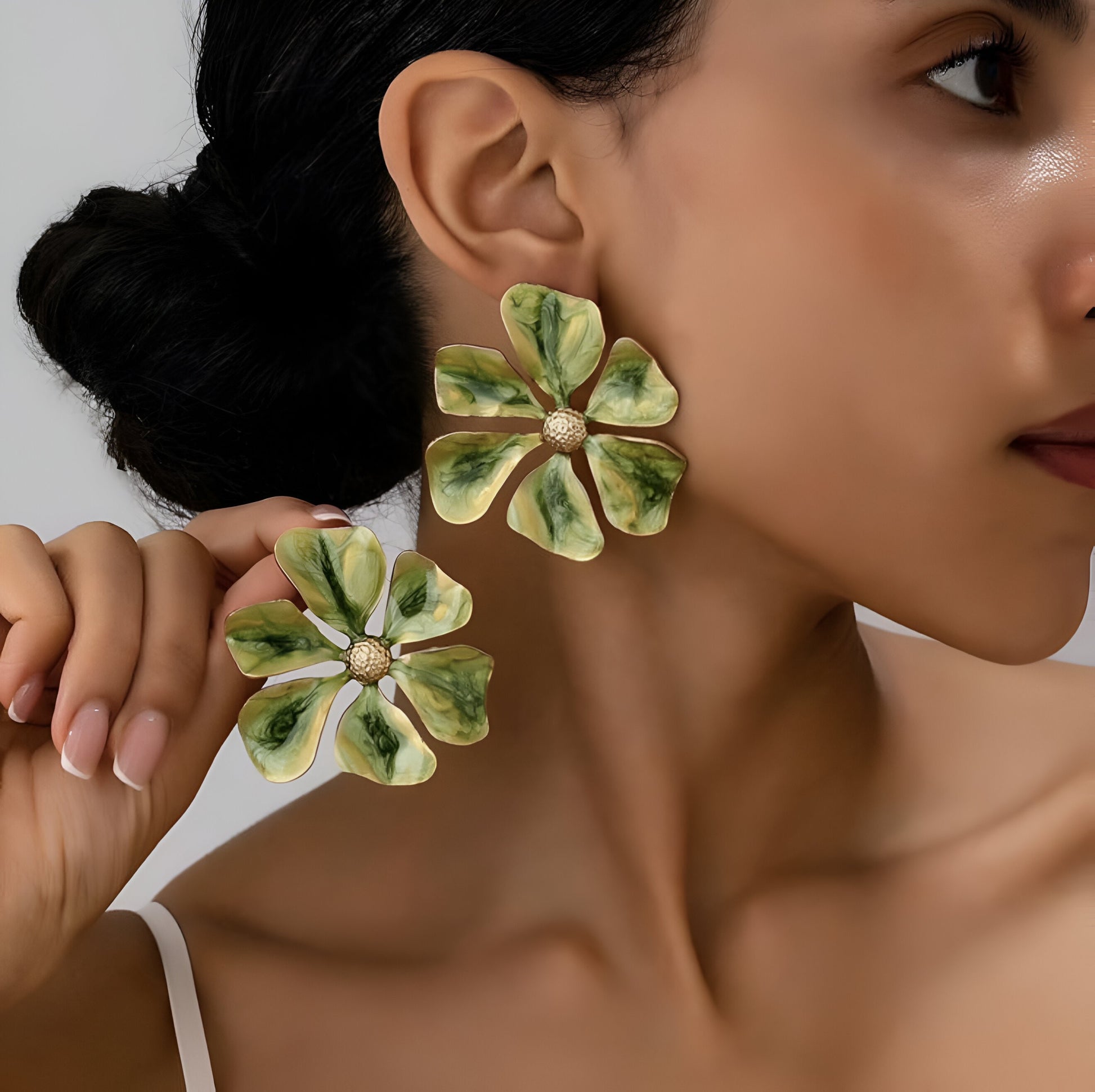 Model wearing large green enamel floral earrings.