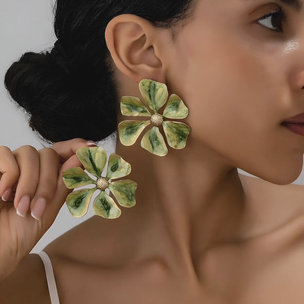 Model wearing large green enamel floral earrings.